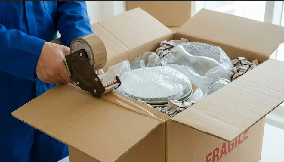 Close-up of a mover sealing a heavy-duty double-wall box containing glassware wrapped in 50mm large-bubble wrap in a Dubai residence.