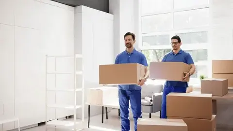 Two male movers carrying large moving boxes, showcasing the physical dimensions that determine the average storage unit cost in Sharjah by size.