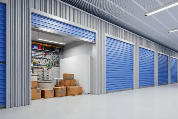 An open, well-lit self-storage unit with blue roll-up doors containing organized boxes and a mattress, representing standard storage unit cost in Sharjah packages.